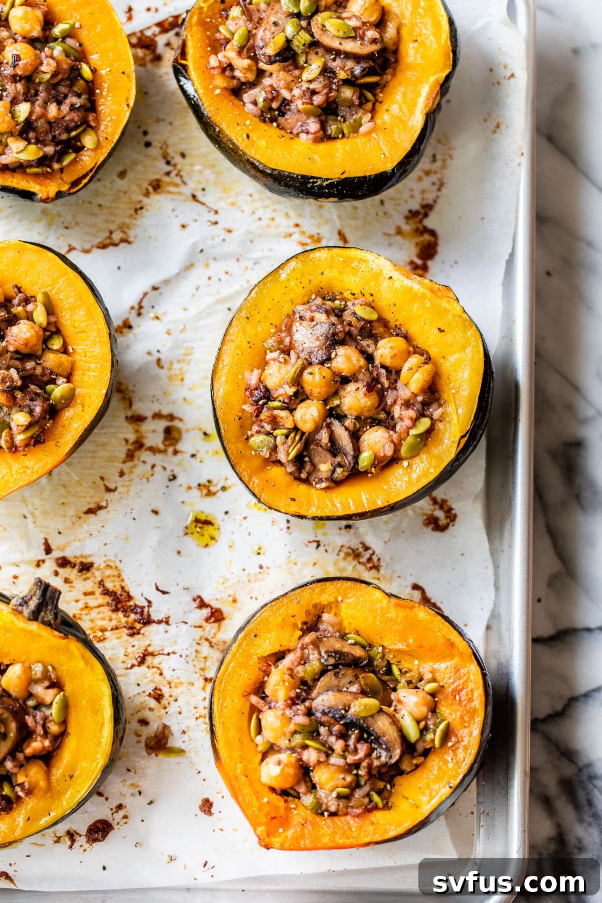 Two halves of baked stuffed acorn squash resting on a baking sheet, ready to be served, showcasing their golden-brown edges and rich filling.