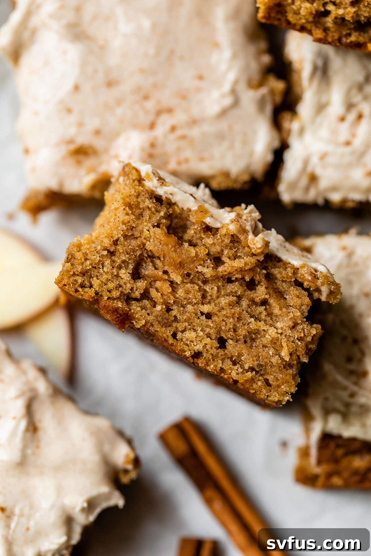 A tantalizing slice of Vegan Apple Cake, lying on its side, showcasing its thick layer of creamy white frosting and the rich, moist texture within.