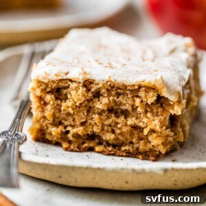a slice of cake with icing on a plate beside an apple