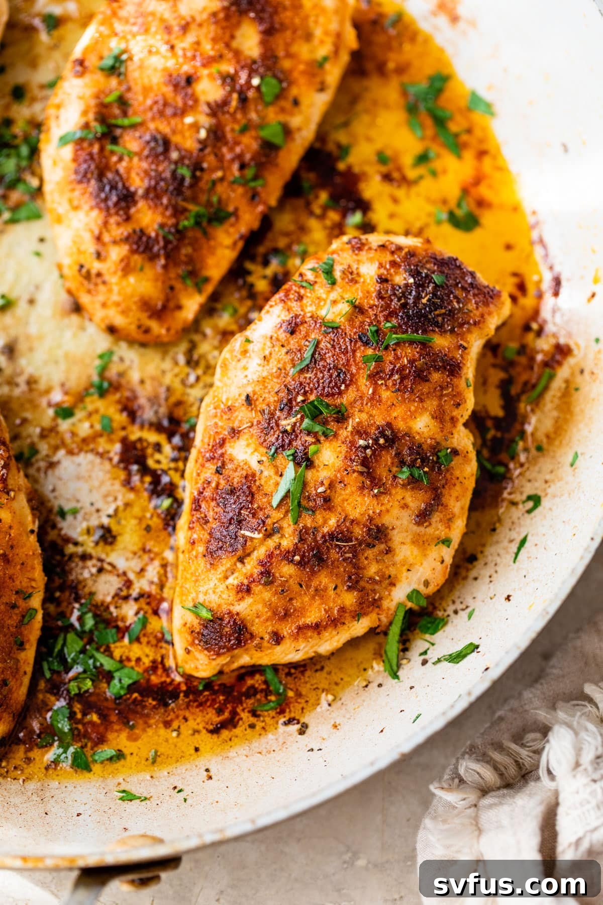 Golden-brown pan-seared chicken breasts sizzling in a hot skillet, garnished with fresh herbs.