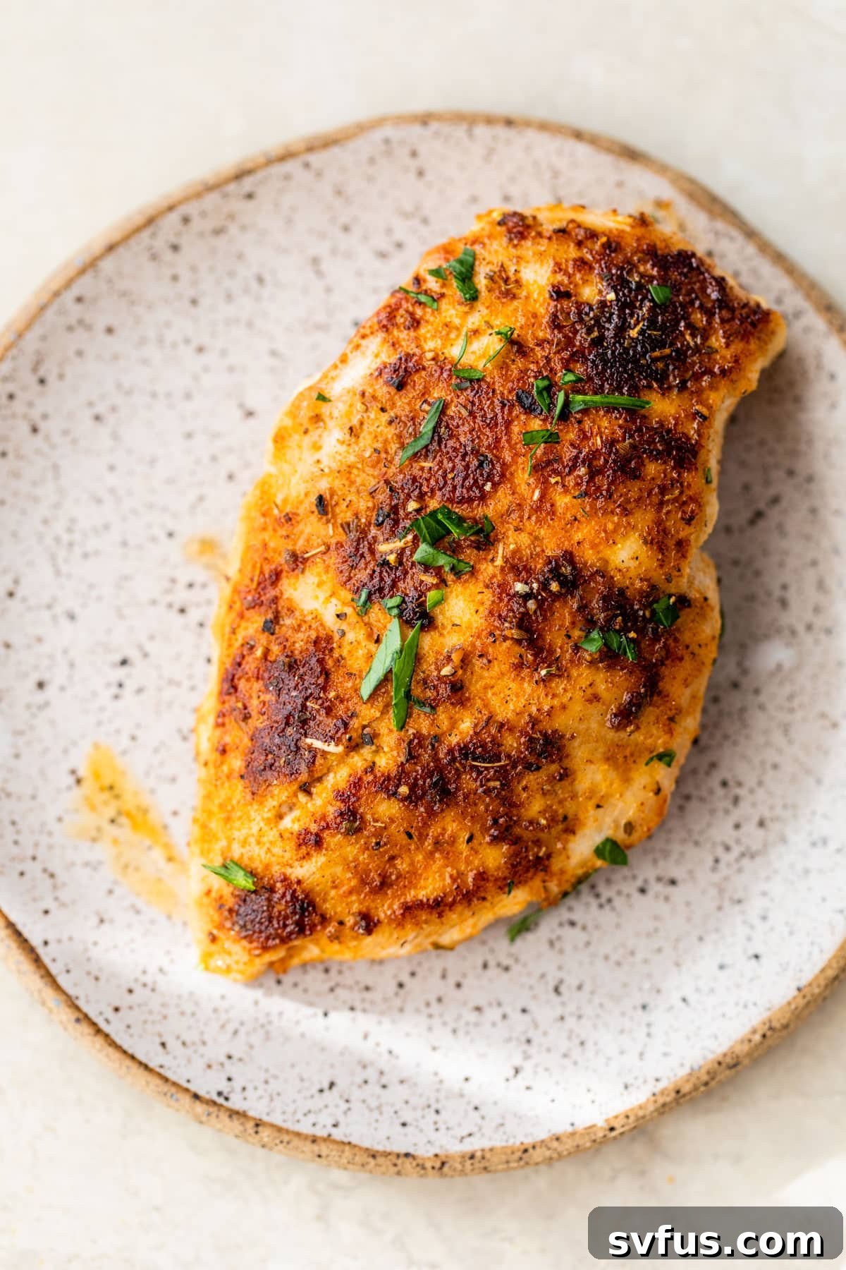 Perfectly seasoned and cooked pan-seared chicken breast, sliced and resting on a small white plate.