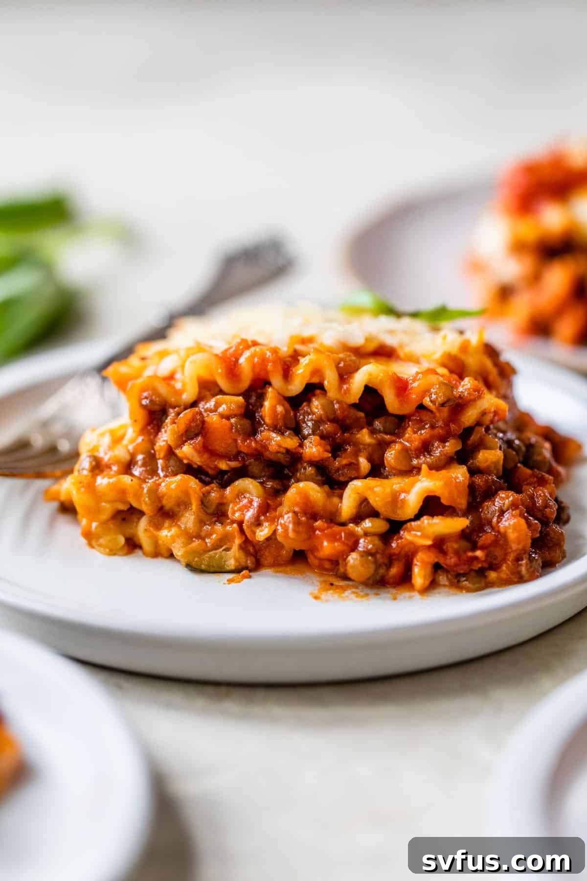 A perfectly portioned slice of vegan lentil lasagna on a white plate, ready to be enjoyed with a fork beside it.