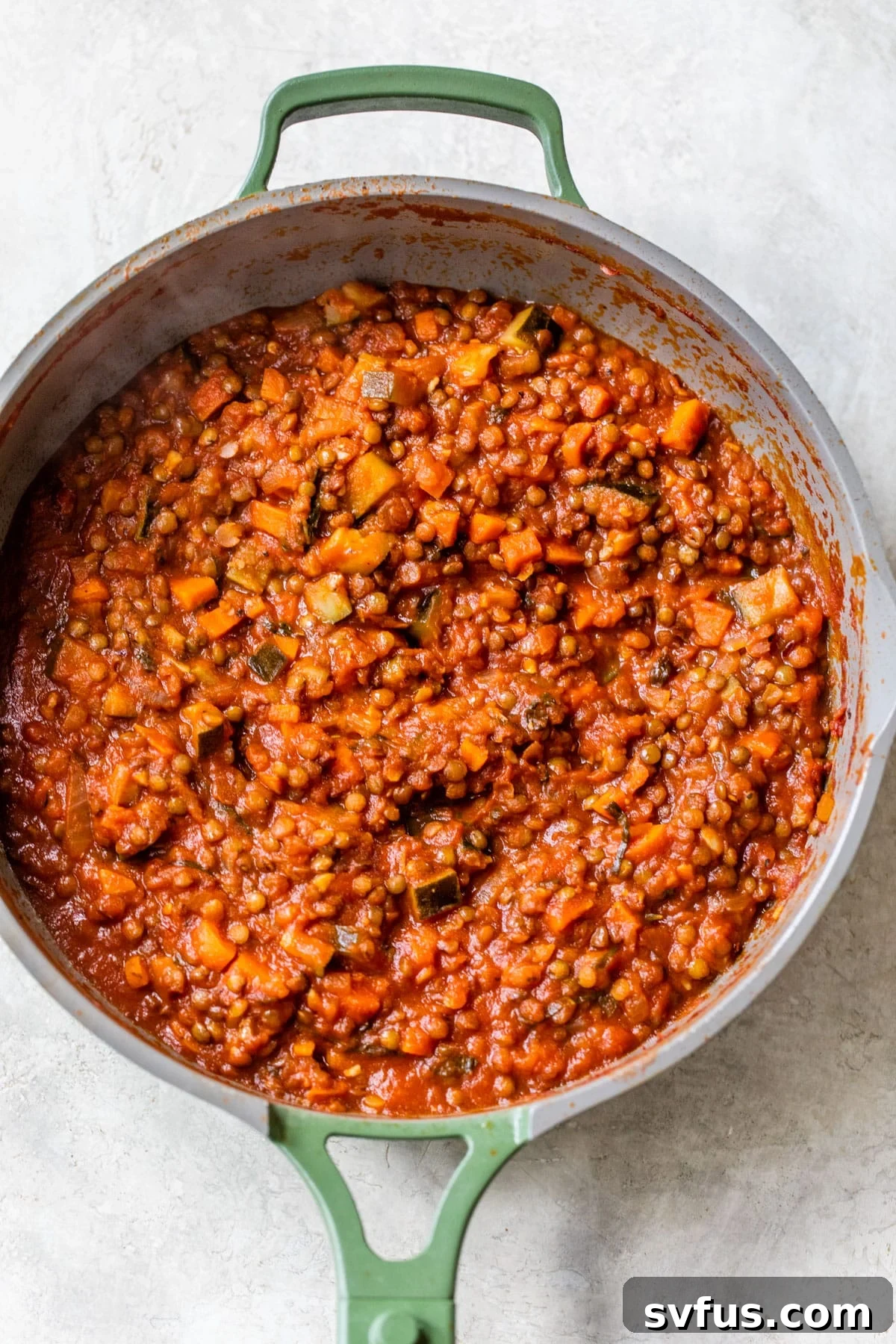 Close-up of the rich lentil mixture with diced vegetables and tomato sauce simmering in a skillet on a stovetop, ready to be incorporated into the lasagna.
