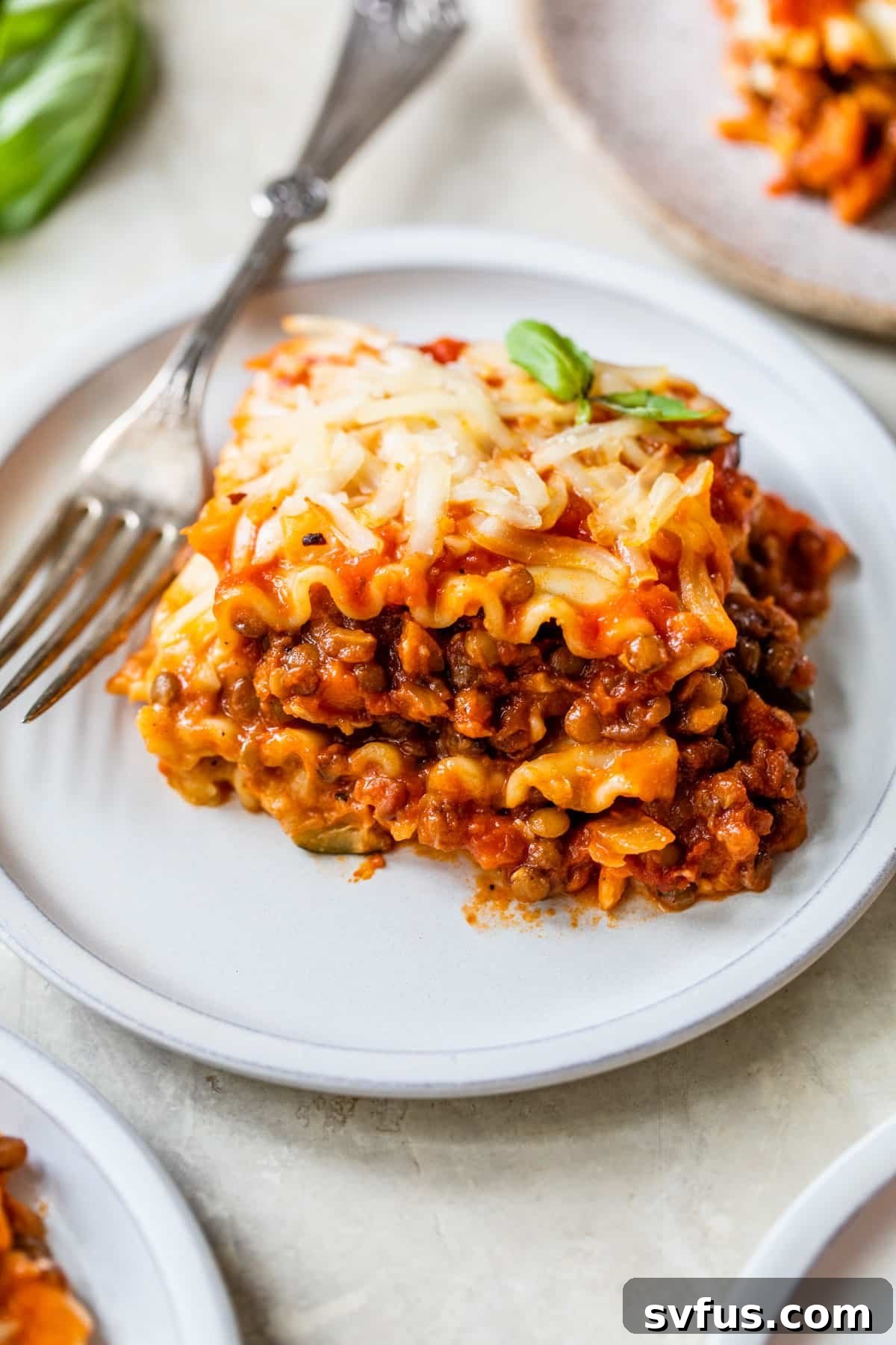 A close-up shot of a single, perfectly cut slice of vegan lentil lasagna on a white plate, with a fork gently piercing it, highlighting the layered goodness.