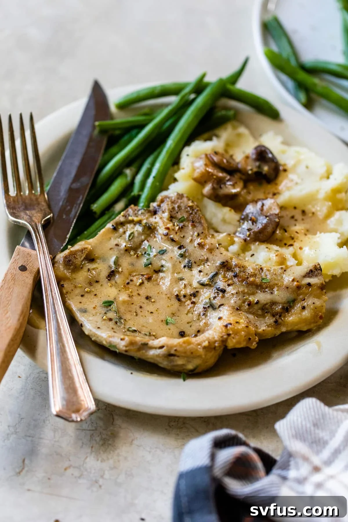 Plated Instant Pot pork chop with mashed potatoes, green beans, and rich mushroom gravy.
