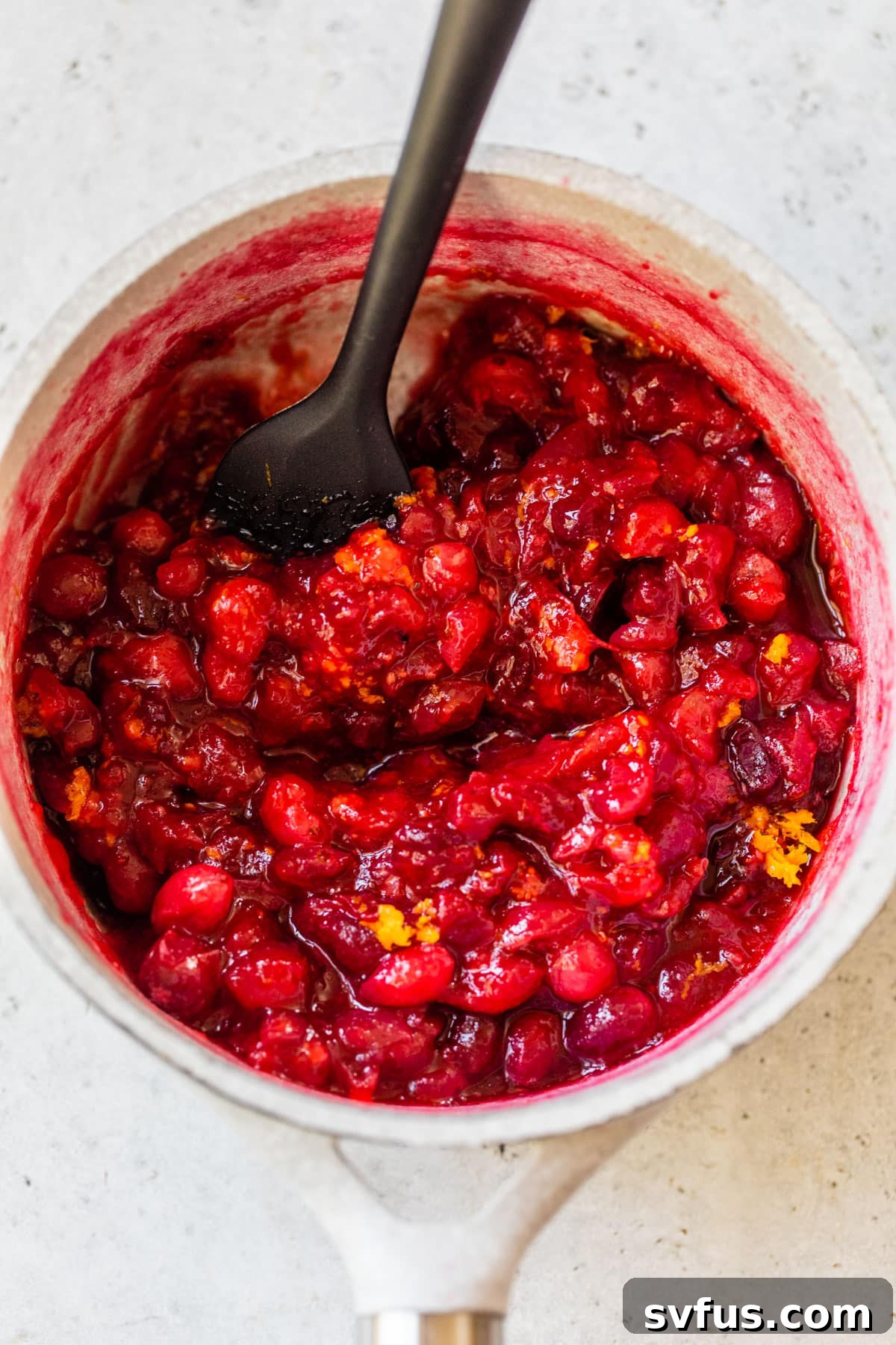 cooked fresh cranberries in a saucepan with a rubber spatula