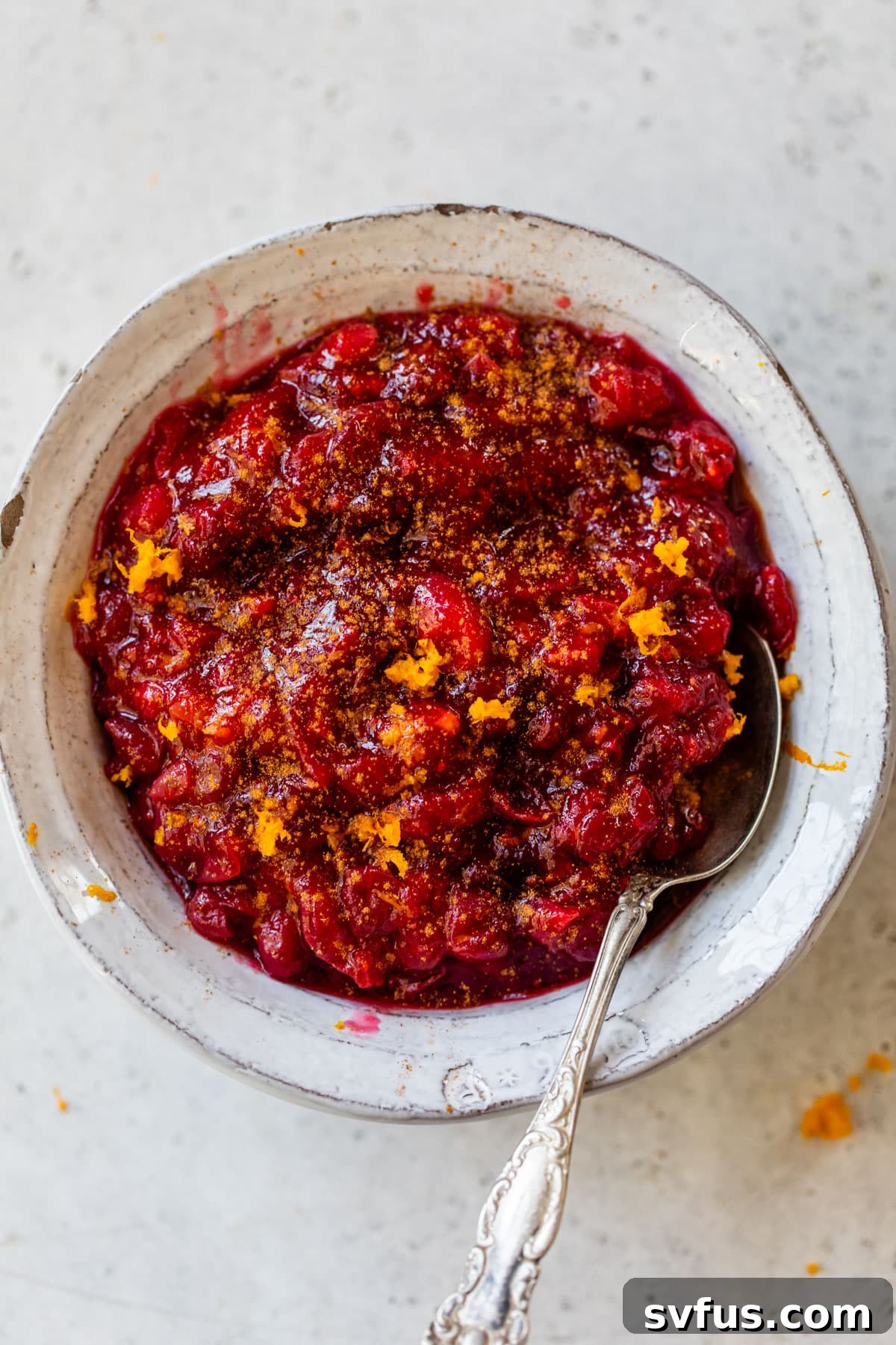 cooked cranberries in a bowl with a spoon topped with orange zest