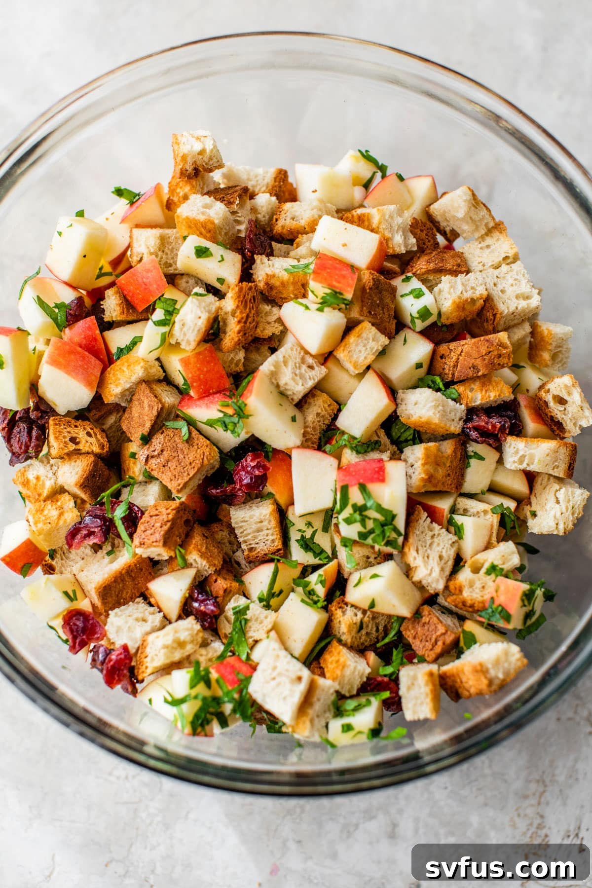 glass bowl with diced apples, toasted gluten-free bread cubes, and fresh parsley