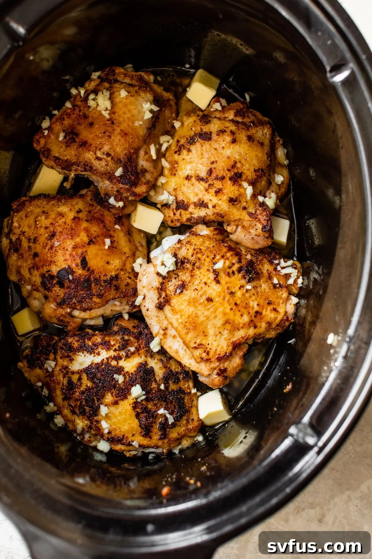 raw chicken thighs in a slow cooker with cubes of butter
