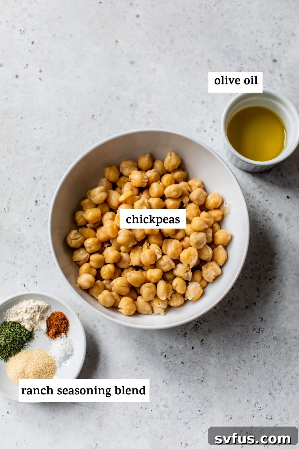 Close-up of ingredients for air fryer chickpeas, including canned chickpeas, olive oil, and a blend of spices like garlic powder, onion powder, and dried dill.