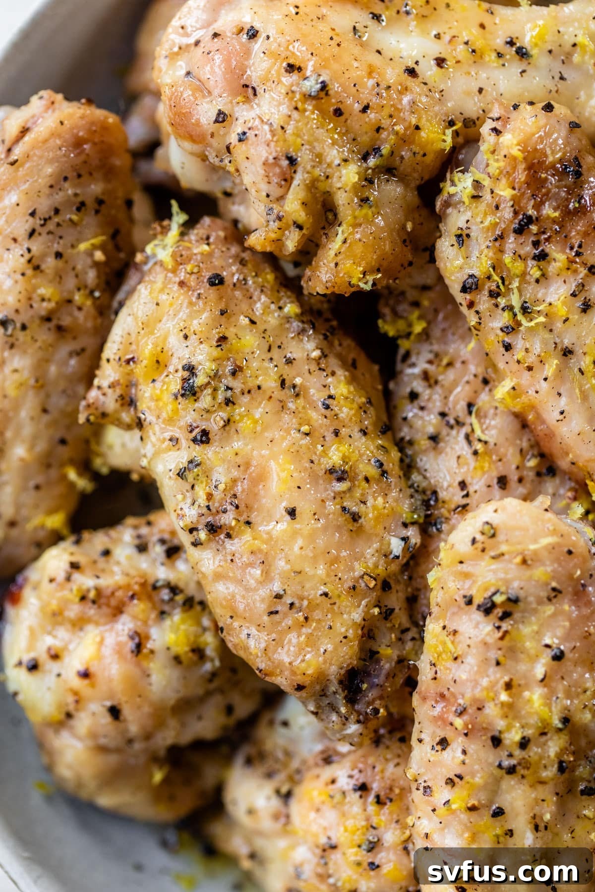 Close up of perfectly crispy baked chicken wings garnished with fresh lemon zest and cracked black pepper, ready to be served.