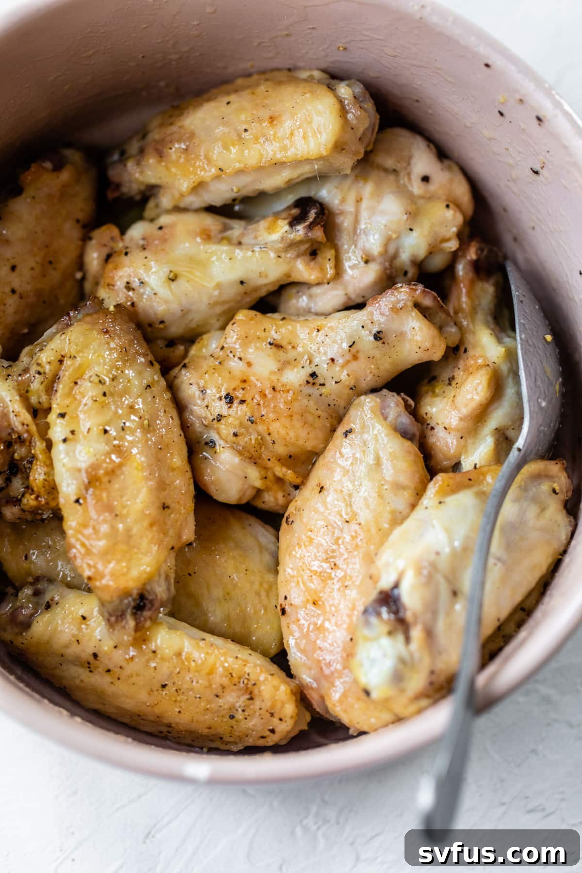 Close up of crispy, golden-brown chicken wings being tossed in a vibrant lemon butter sauce within a large mixing bowl.