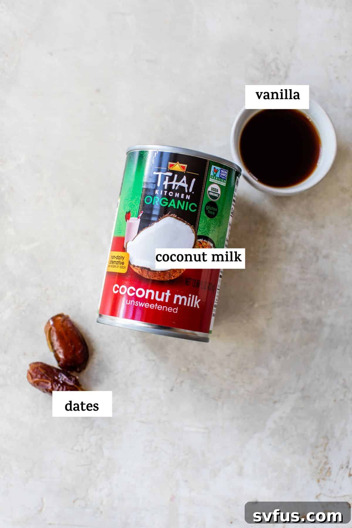 Three key ingredients for paleo coffee creamer: a can of full-fat coconut milk, pitted dates, and a bottle of vanilla extract, artfully arranged on a light surface.