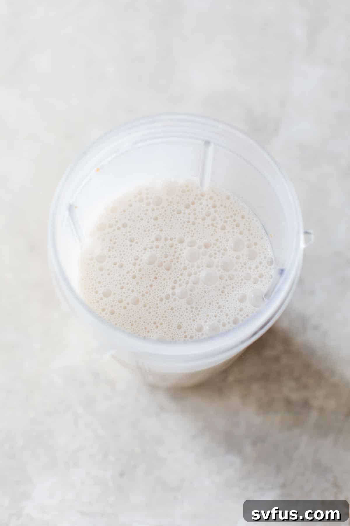 A high-speed blender actively blending white, creamy coconut milk, dates, and vanilla extract, creating a smooth paleo coffee creamer.