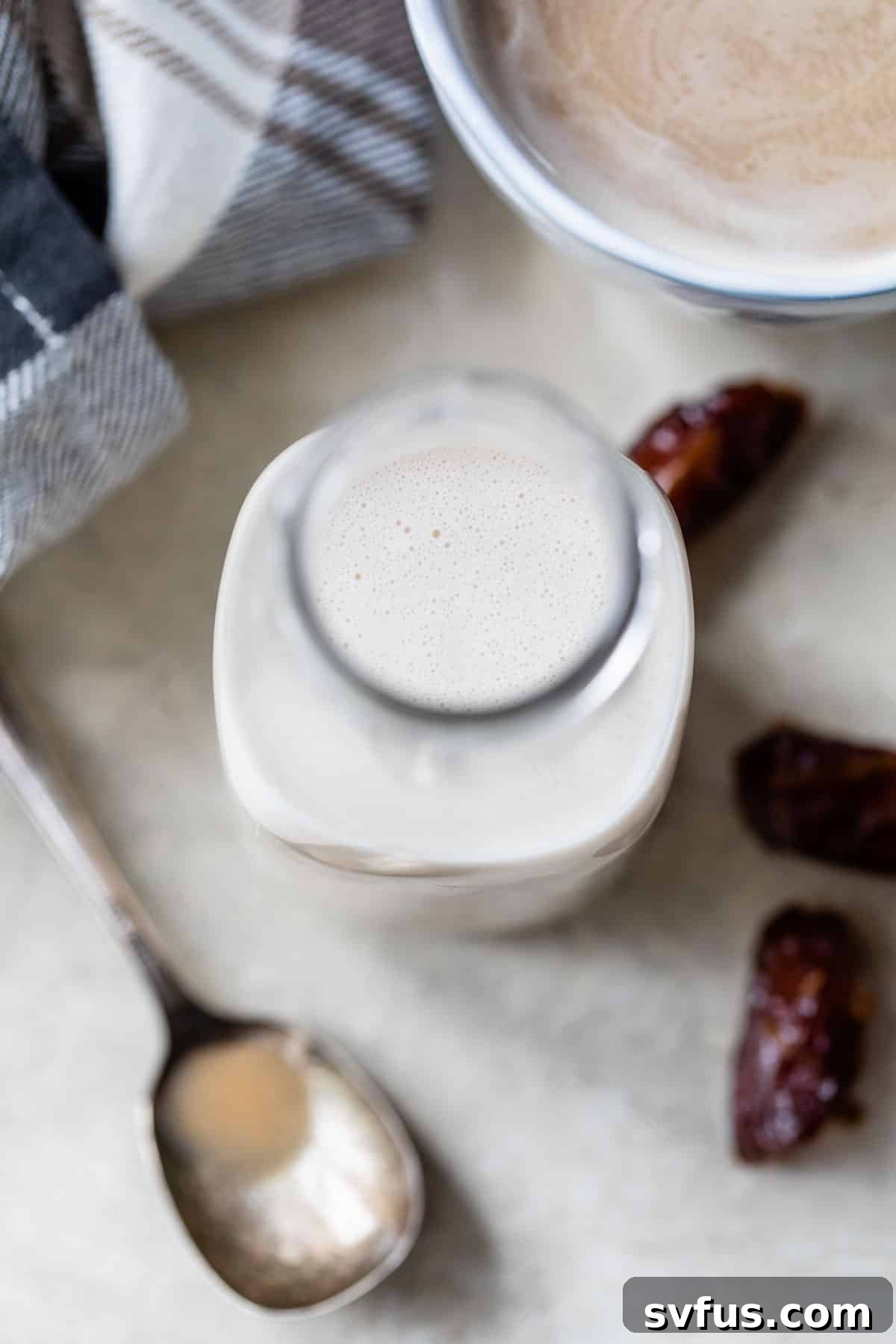 A glass jar filled with creamy paleo coffee creamer, placed next to a mug of coffee and two fresh dates on a rustic wooden surface.