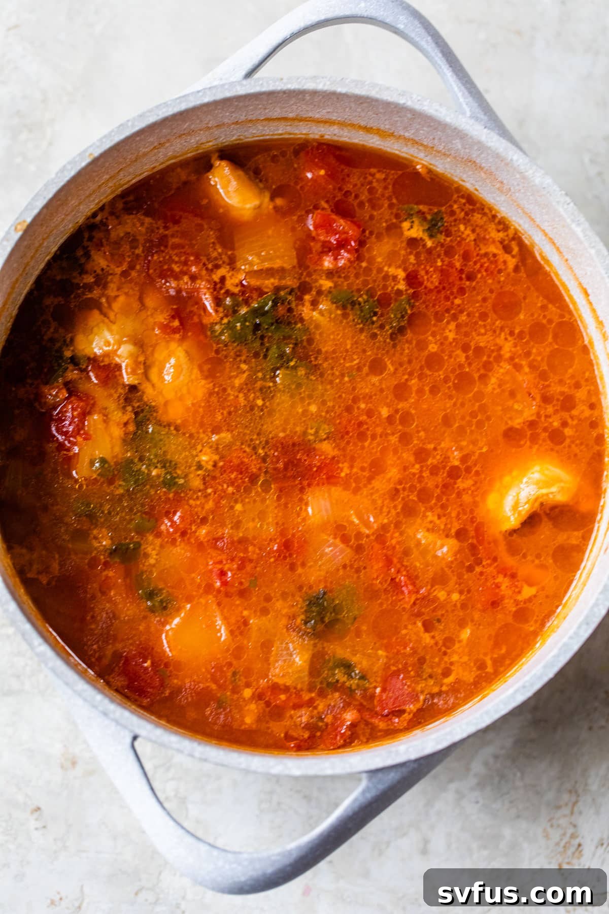 Large pot simmering with chicken thighs, diced tomatoes, chopped onion, and fresh cilantro, forming the base of the pollo guisado.