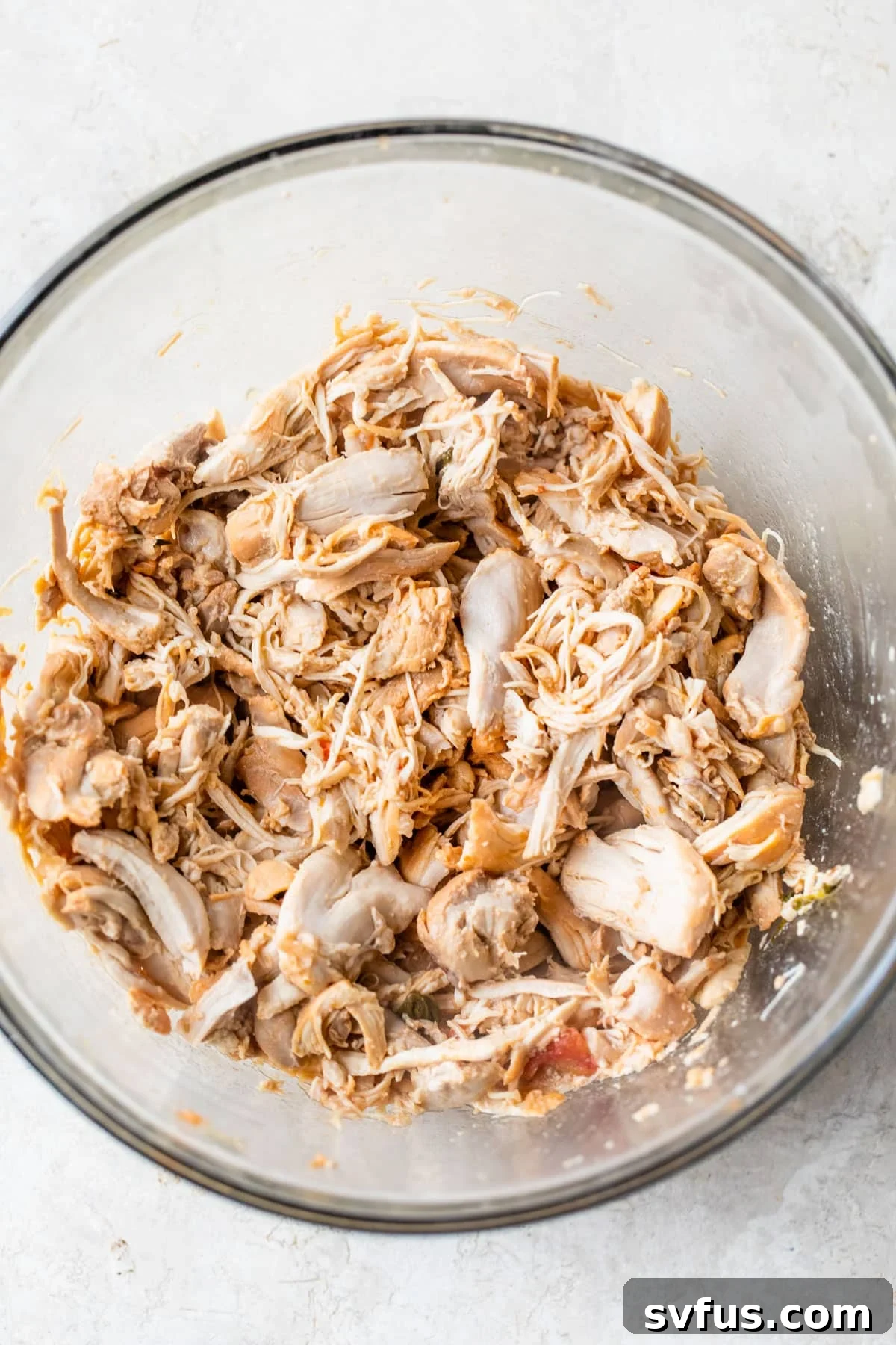A large glass bowl filled with perfectly shredded chicken, ready for assembly into the Panes con Pollo sandwich.