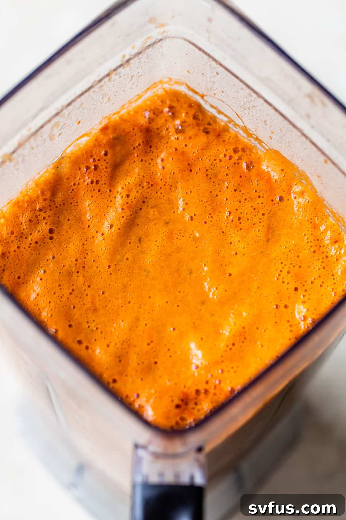 A blender containing the vibrant, orange-colored Salvadoran salsa, made from the chicken stock, fresh tomatoes, bell pepper, onion, and cilantro.