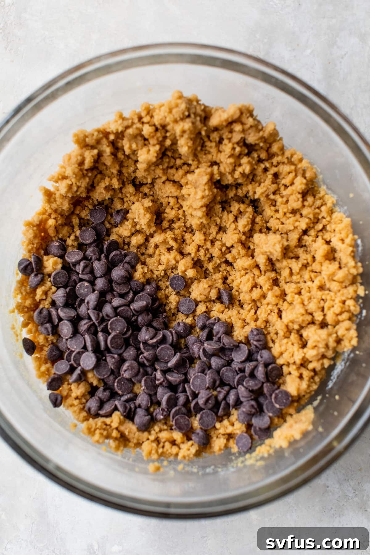 Close-up of thick, rich vegan cookie dough in a mixing bowl, generously studded with chocolate chips, ready for baking.