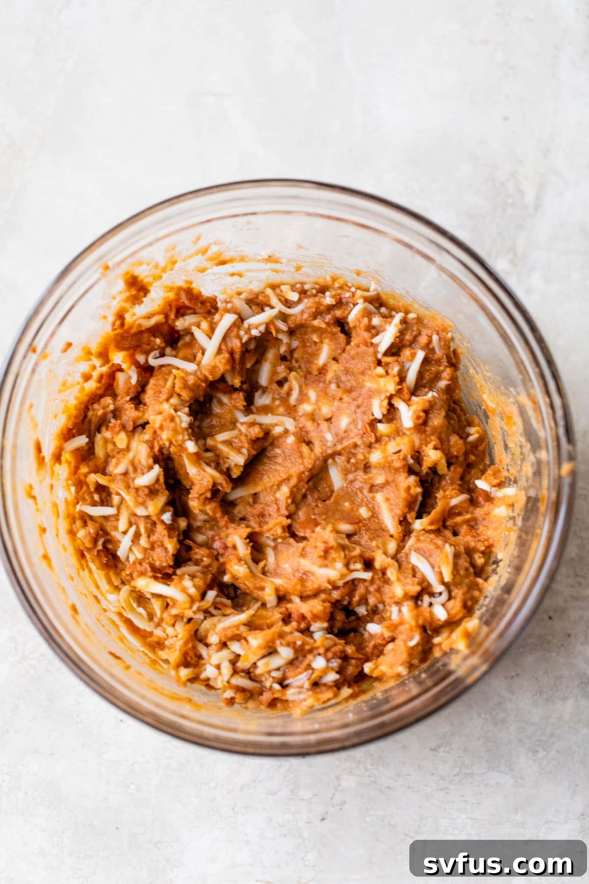a glass bowl filled with refried beans and shredded cheese