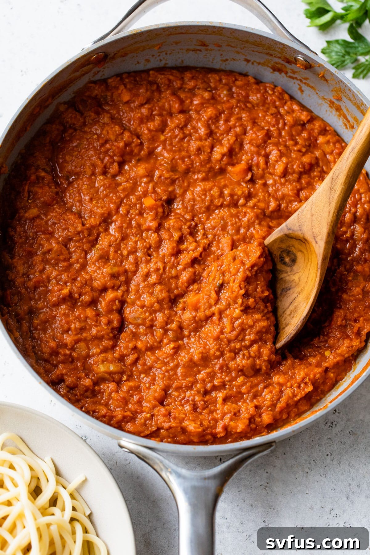 A close-up shot of the rich, simmering lentil ragu in a skillet, with a wooden spoon resting in the sauce, inviting you to taste.