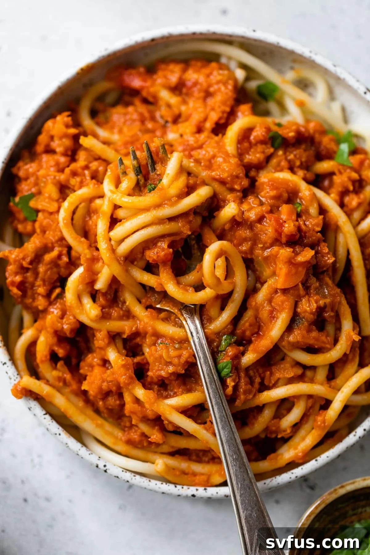 A fork twirled around spaghetti generously coated in rich lentil ragu, ready to be enjoyed, highlighting the sauce's perfect consistency.