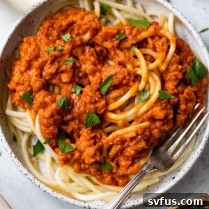 A bowl of pasta with sauce and chopped parsley beside a glass of white wine
