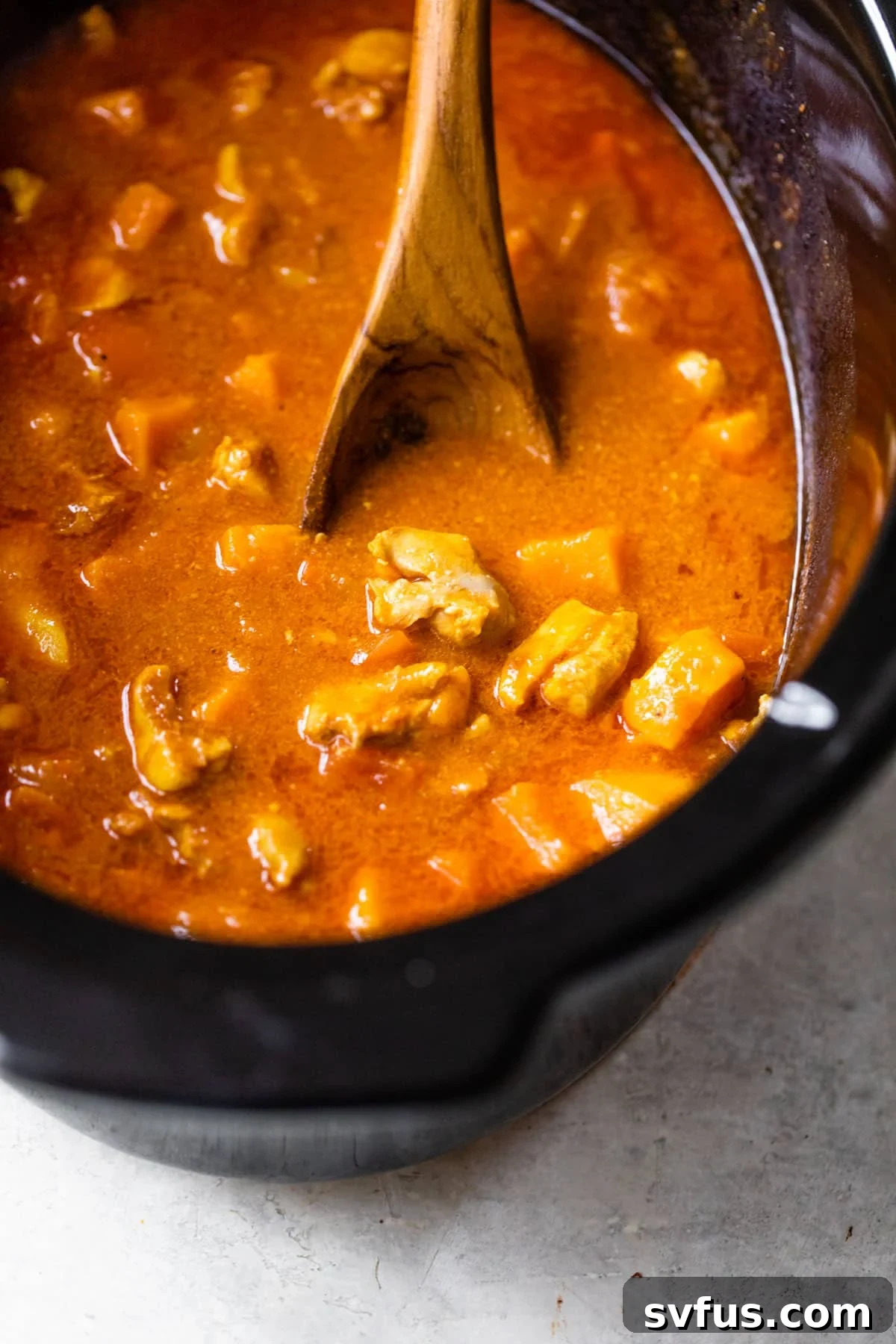 slow cooker with cut cooked chicken and a wooden spoon in broth
