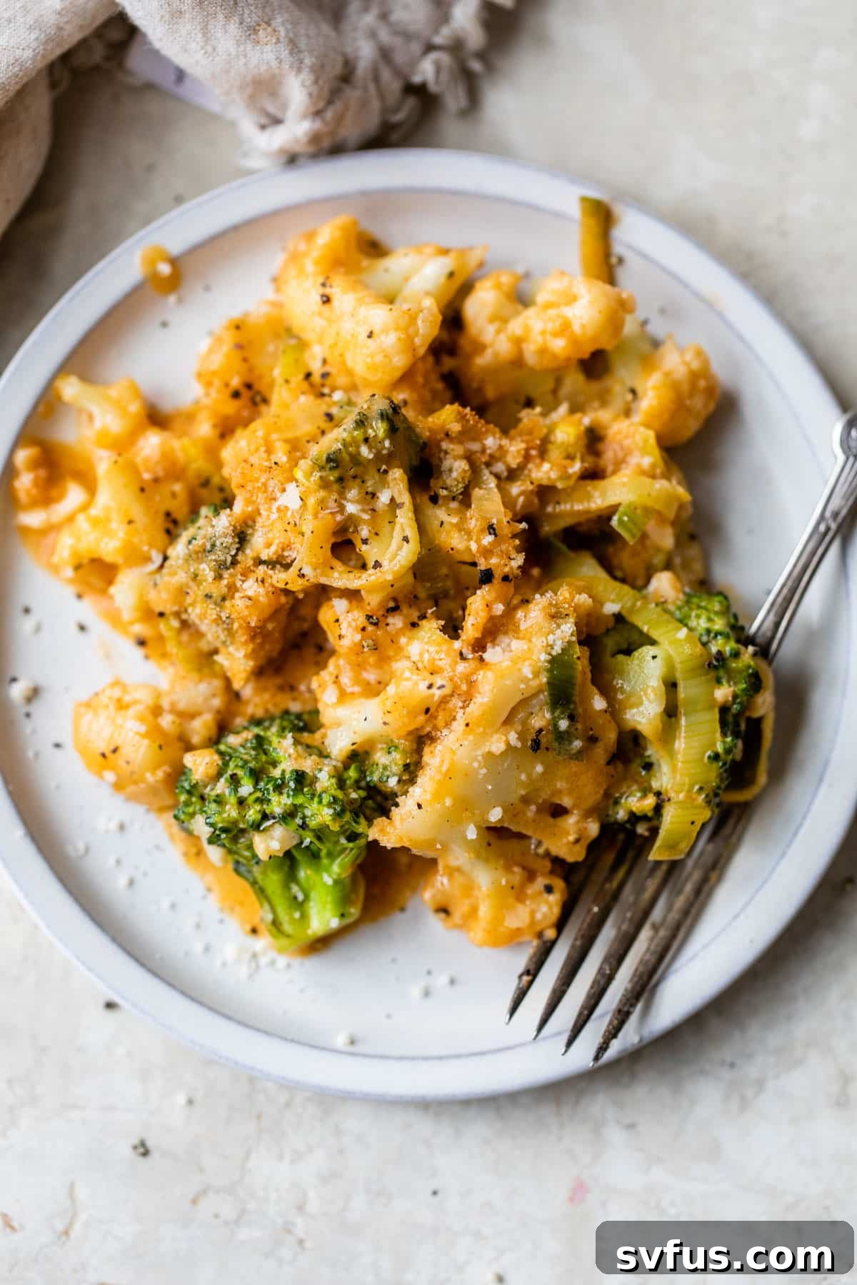 A plate of creamy broccoli and cauliflower casserole, garnished with fresh herbs, with a fork ready to dig in.