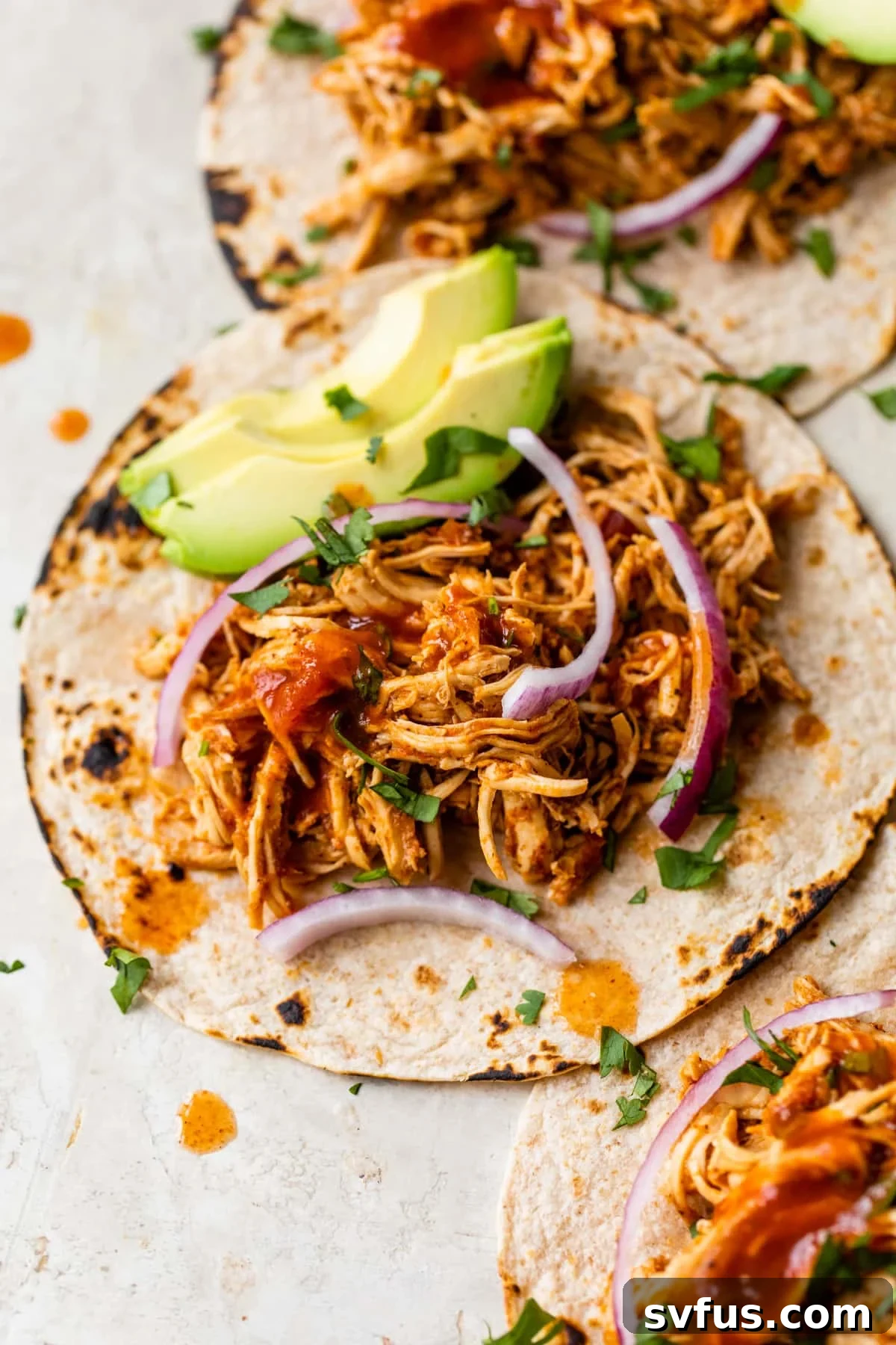 Flavorful shredded chicken tacos topped with fresh red onion and creamy avocado, served on a plate.