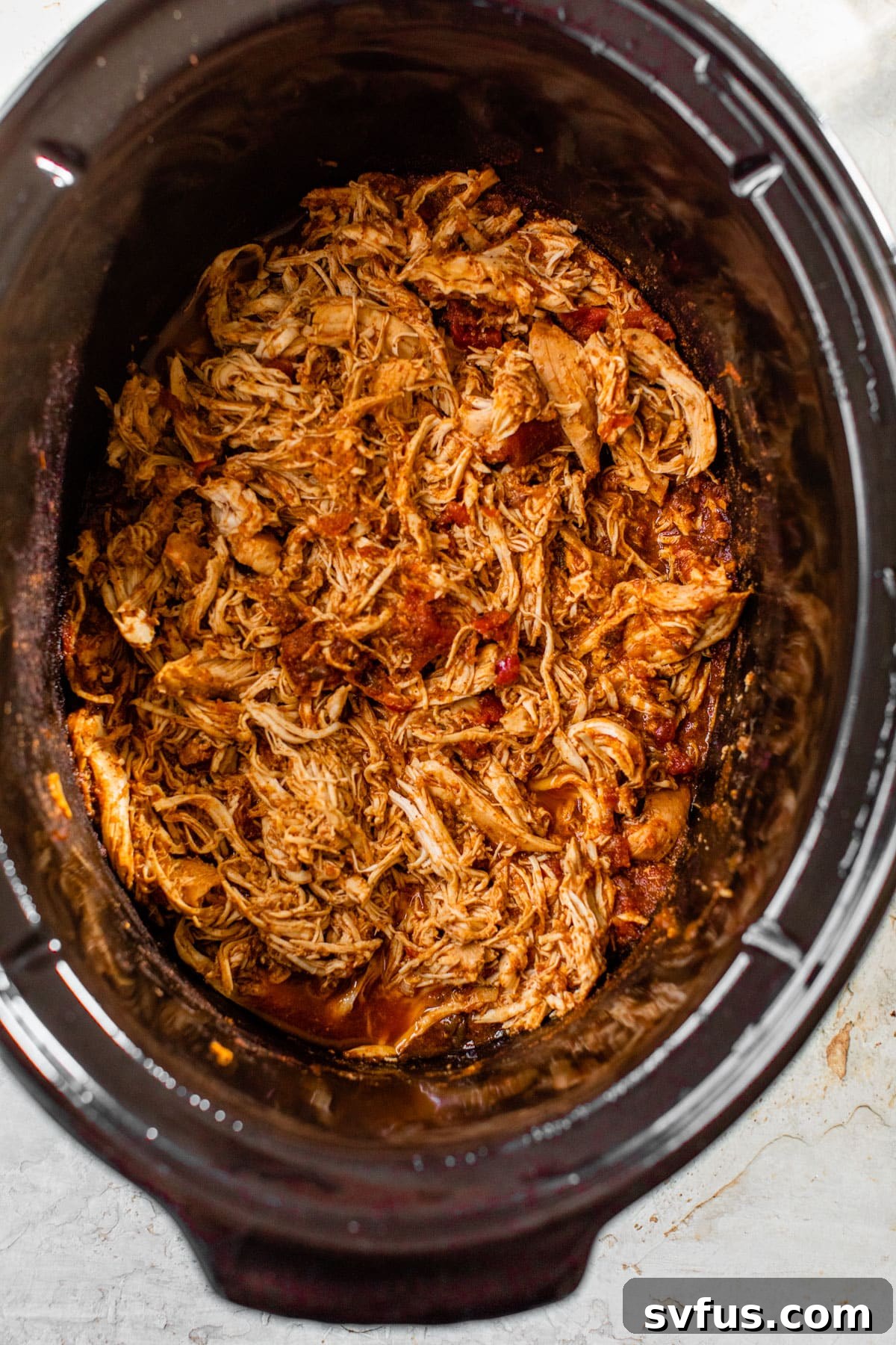 Close-up of shredded, cooked chicken immersed in a vibrant red sauce within the slow cooker.