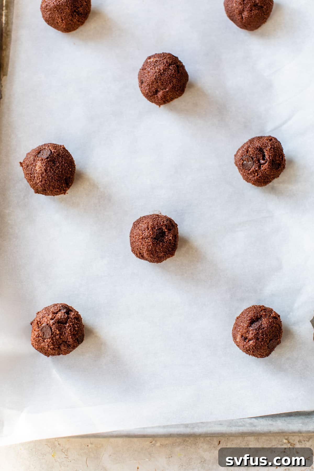 Rows of chocolate cookie dough balls neatly arranged on a parchment-lined baking sheet, ready for the oven.