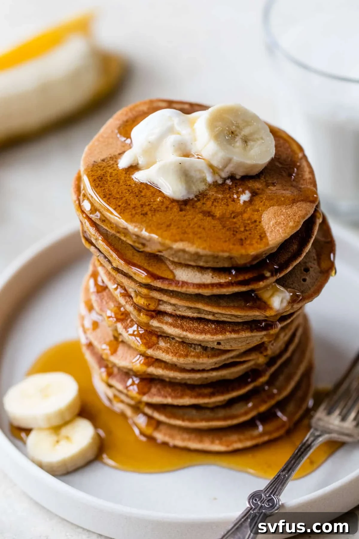 stack of fluffy banana yogurt pancakes on a plate topped with creamy yogurt and fresh banana slices, drizzled with maple syrup