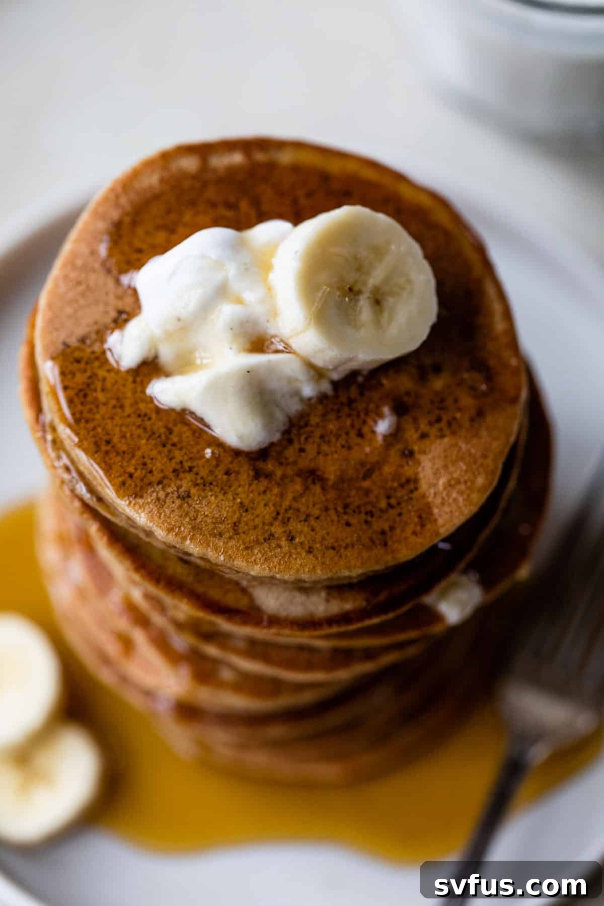 a delightful stack of golden-brown banana yogurt pancakes on a white plate, generously drizzled with rich maple syrup and adorned with fresh banana slices