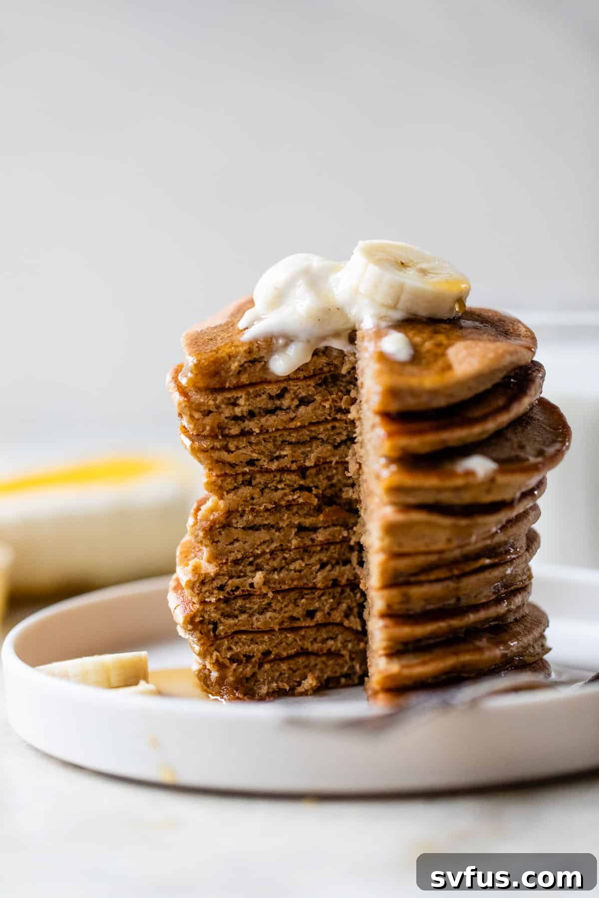 a stack of freshly cooked banana yogurt pancakes, with one pancake cut to reveal its fluffy interior