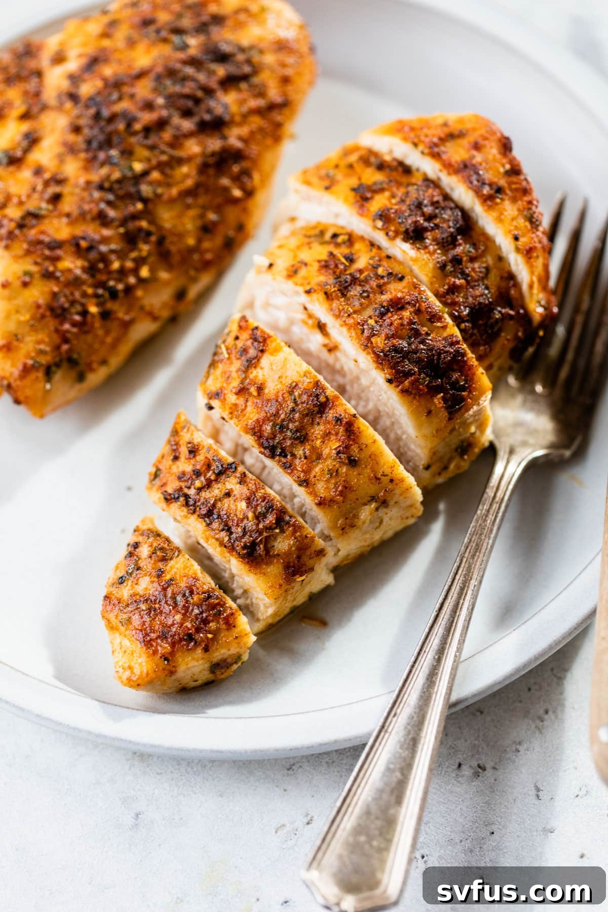 perfectly sliced cooked chicken breast on a plate next to a fork, revealing its juicy interior