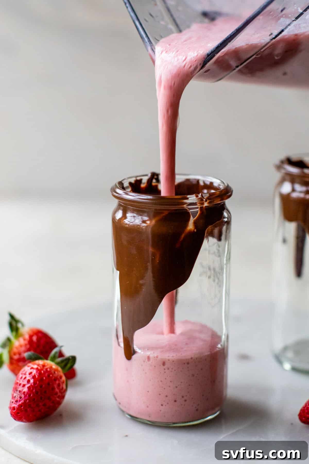 someone pouring a pink smoothie from a blender into a glass