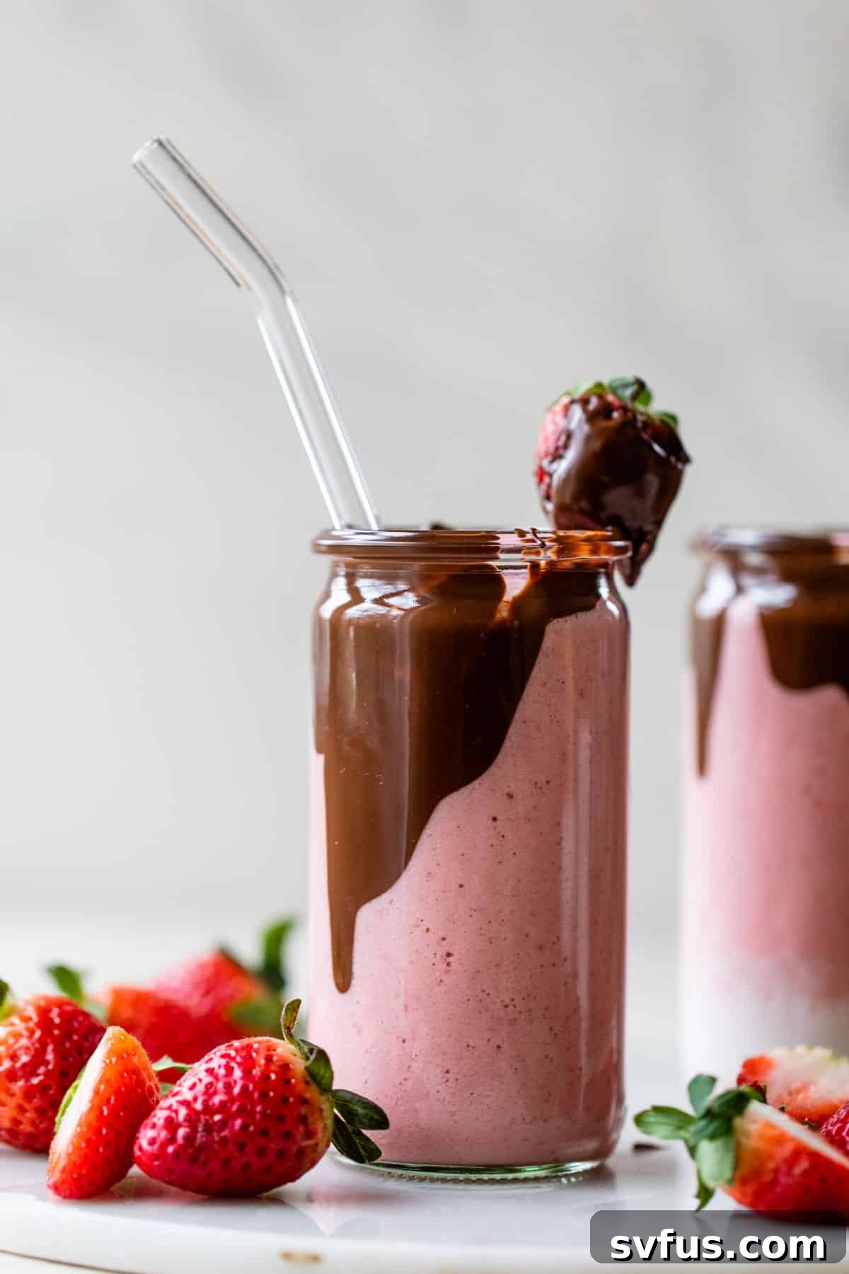 glass filled with a pink-colored smoothie with chocolate on the inside and a chocolate covered strawberry on top
