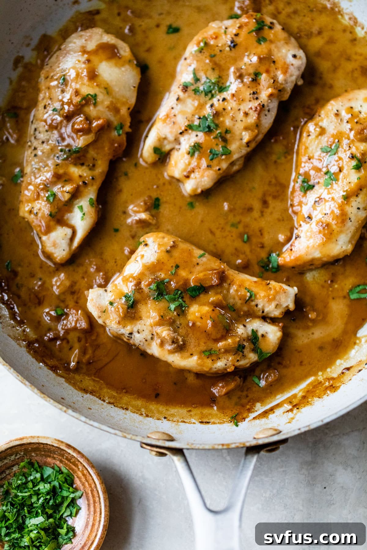 A large cast iron skillet filled with four perfectly cooked chicken breasts, submerged in a rich, dark golden-brown creamy garlic sauce.