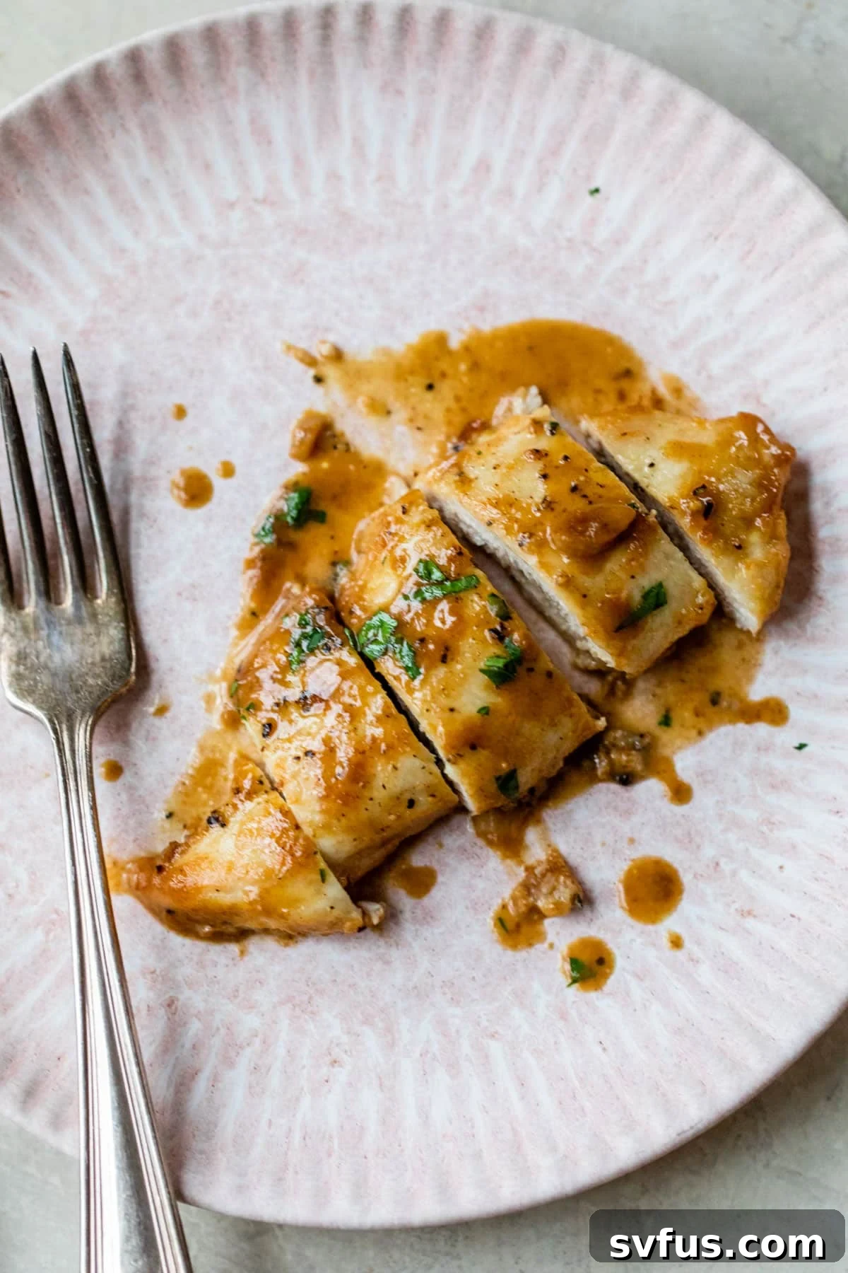 A single perfectly cooked chicken breast served on a white plate, drizzled with creamy garlic sauce and accompanied by a fork.