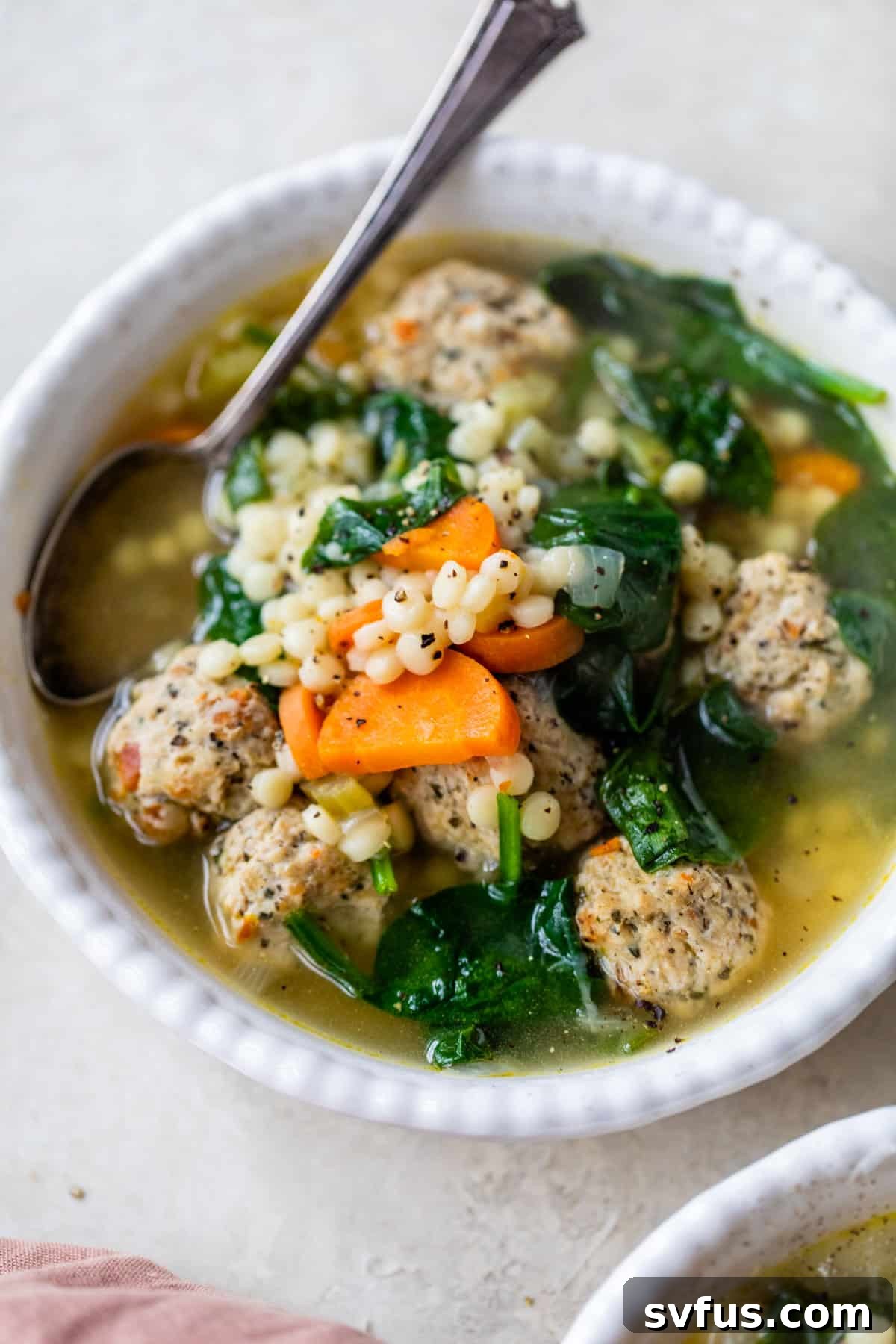 A beautiful bowl of Instant Pot Italian Wedding Soup, with a spoon ready for a bite, showcasing the rich broth, tender meatballs, and vibrant greens.