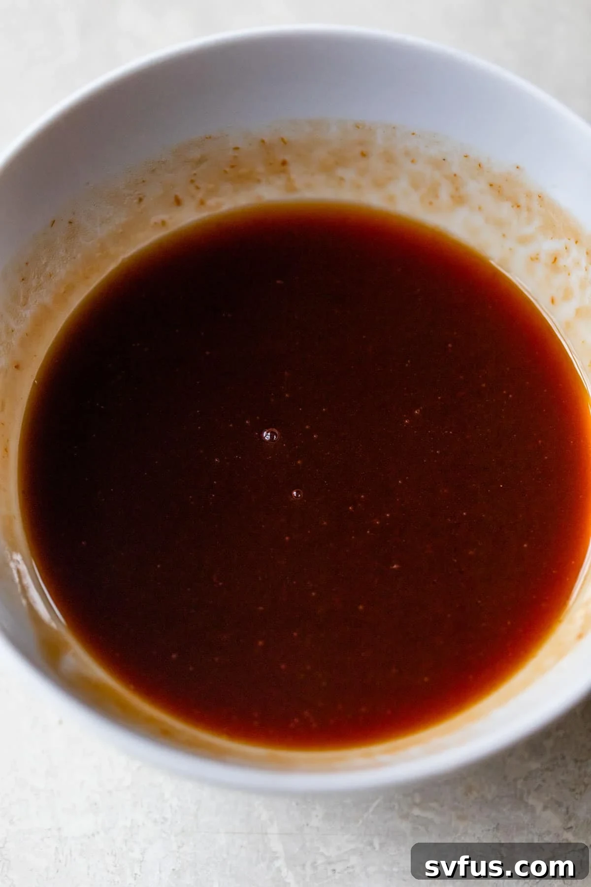 A small glass bowl filled with a reddish-brown sweet and sour sauce, ready to be used.