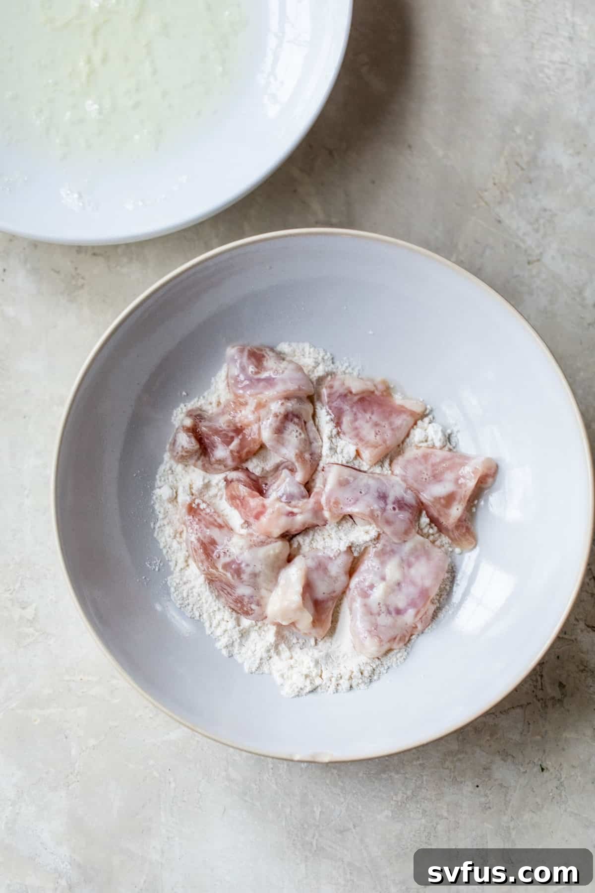 A bowl filled with raw chicken pieces, lightly coated in flour, prepared for cooking.
