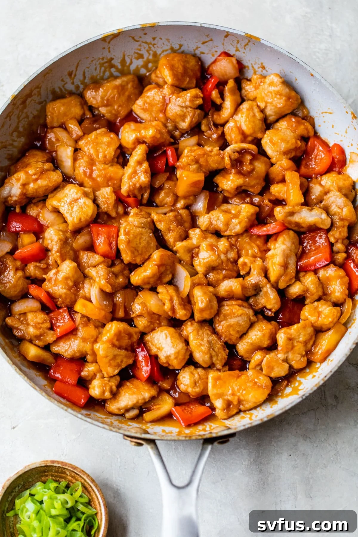 A skillet filled with deliciously coated sweet and sour chicken, vibrant bell peppers, and pineapple chunks.