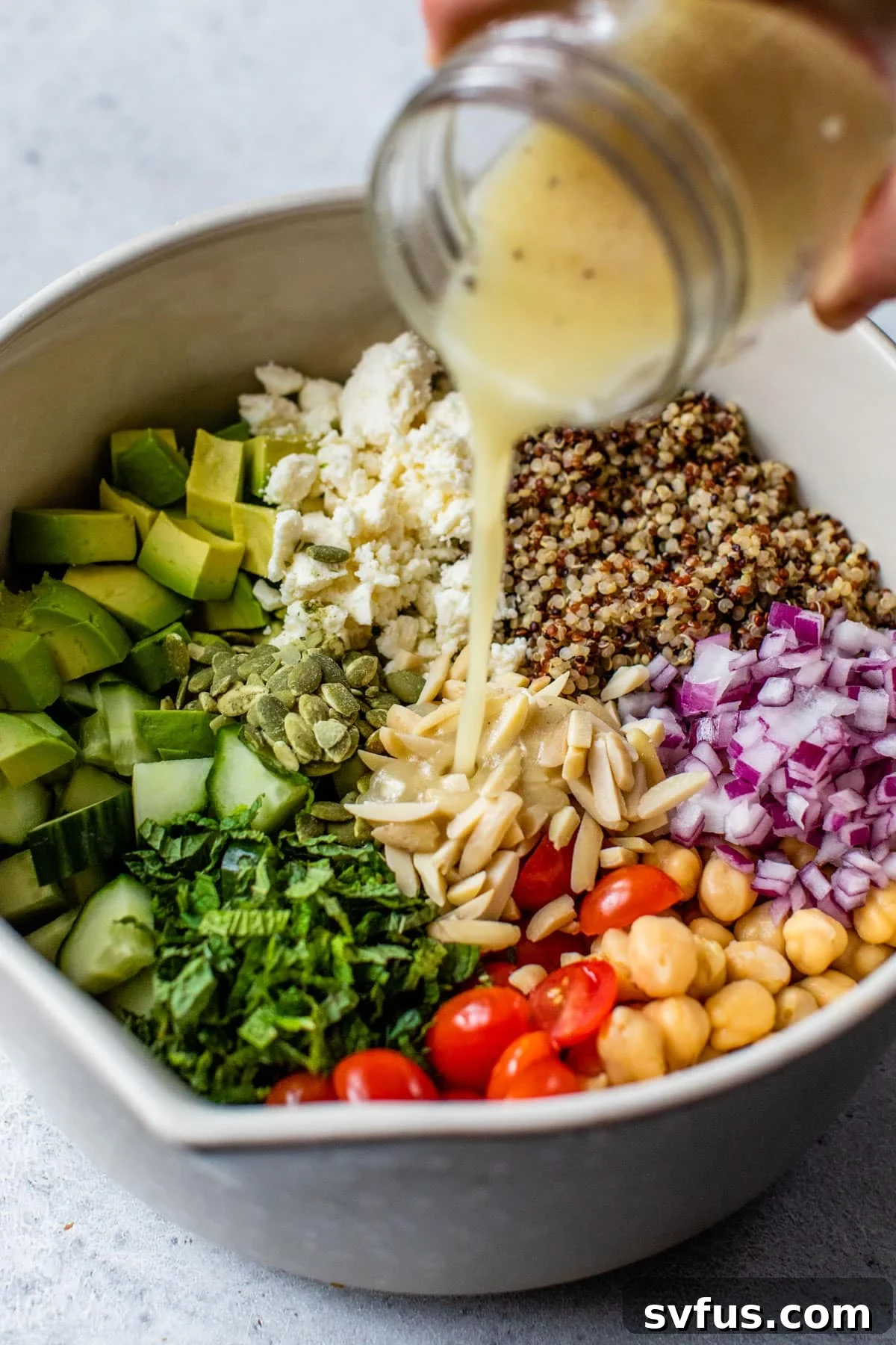 A close-up shot of the Zesty Quinoa Salad in a bowl, with the tangy homemade dressing being poured over the top, highlighting the fresh ingredients before mixing.