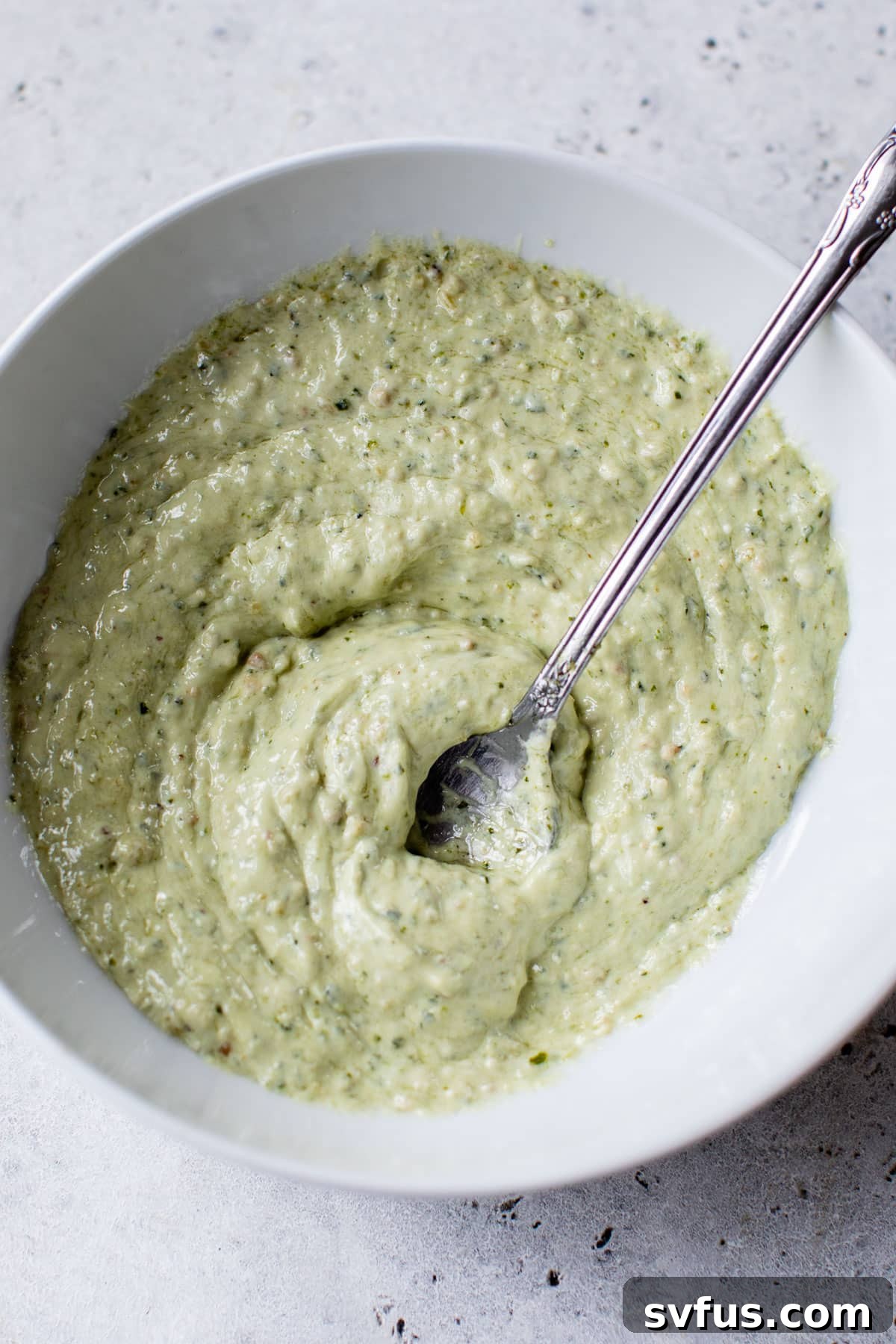 Creamy pesto, Greek yogurt, and mayonnaise dressing mixed in a bowl for Pesto Chicken Salad.