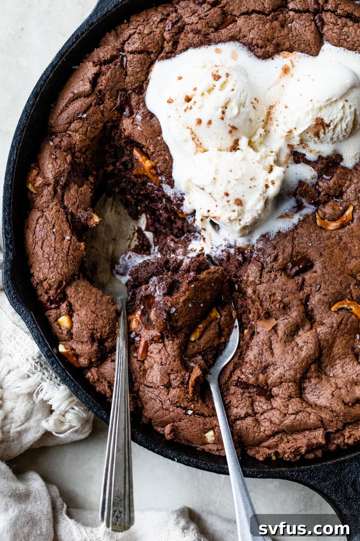 Close-up of two spoons digging into a chocolate skillet cookie with vanilla ice cream