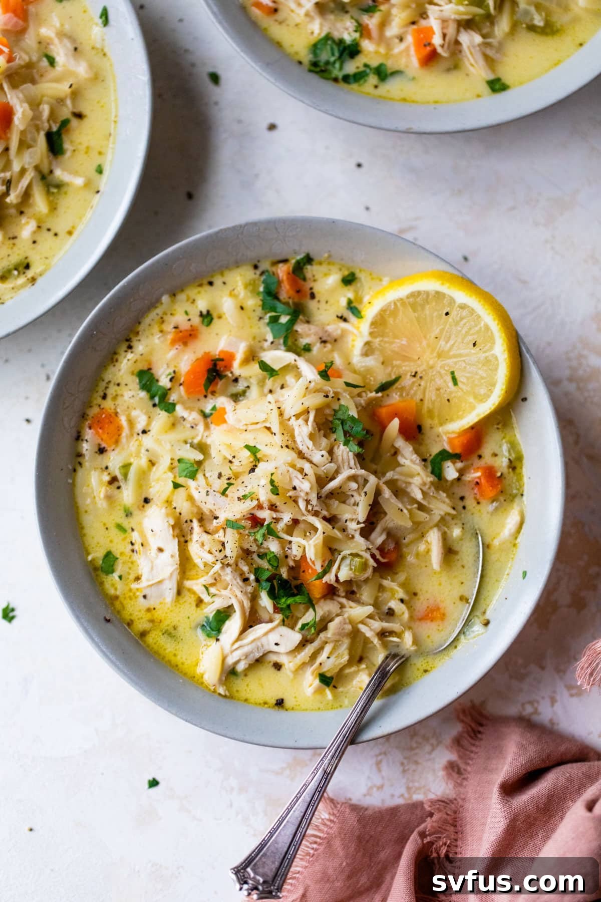 A steaming bowl of creamy lemon chicken orzo soup, garnished with fresh parsley and a spoon, ready to be enjoyed.