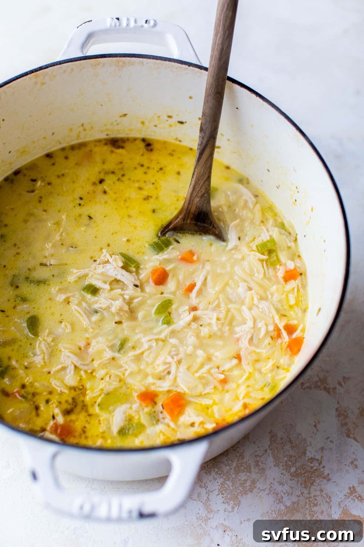 Close-up shot of a Dutch oven filled with simmering chicken orzo soup, showing the creamy texture with vegetables, chicken, and orzo, just after the heavy cream has been added.