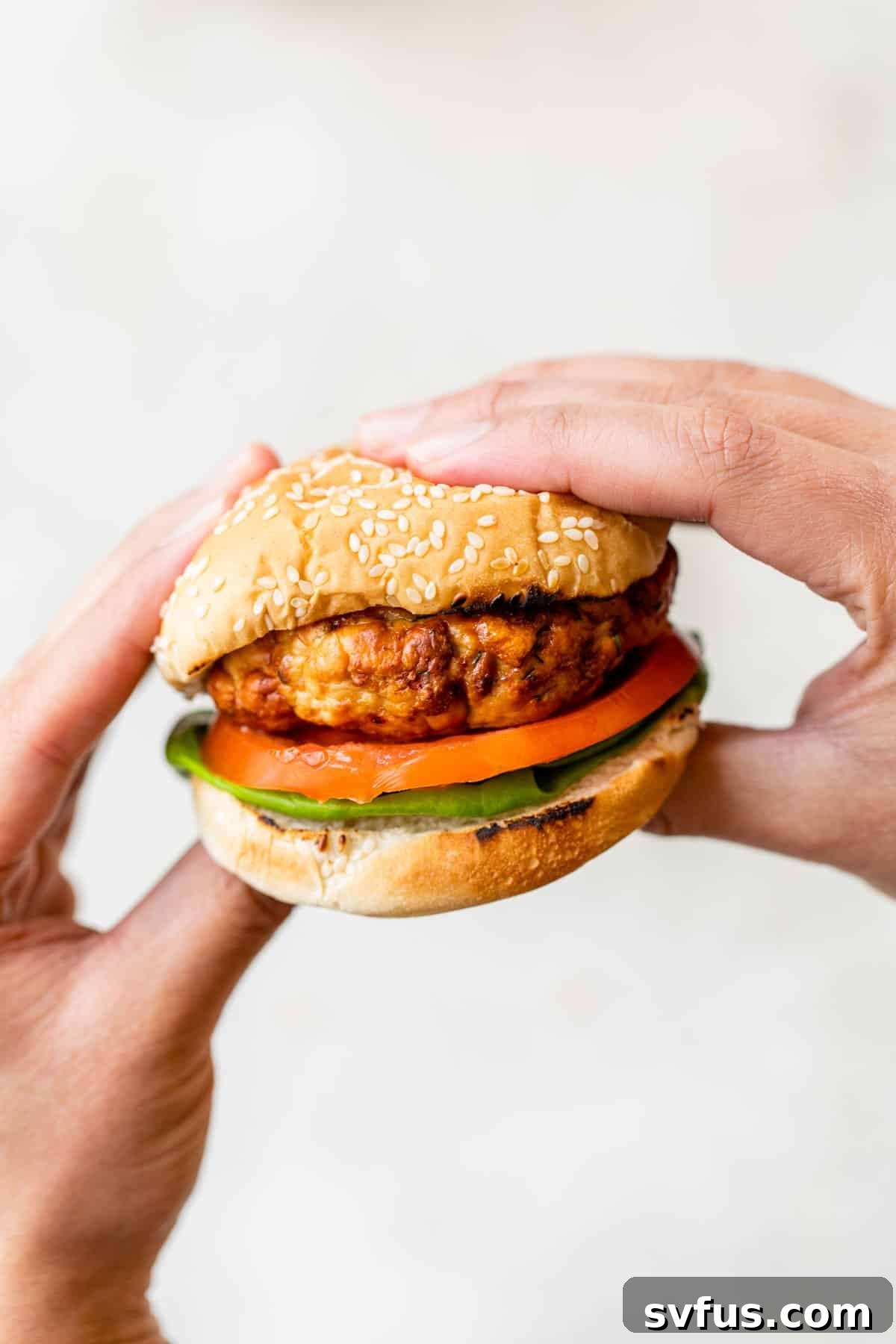 two hands holding a turkey burger sandwich with a bun, lettuce, tomato, and red onion